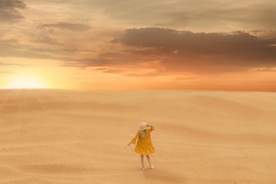 Woman in sandy desert at sunset, back view