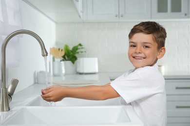 Boy holding hands under water running from tap in kitchen
