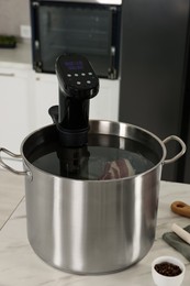 Photo of Pot with sous vide cooker on table indoors. Thermal immersion circulator