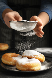 Woman decorating delicious donuts with powdered sugar at black table, closeup