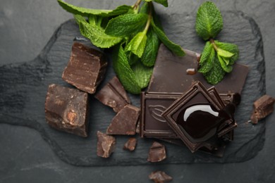 Tasty chocolate pieces with syrup and mint on black table, flat lay