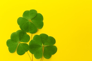 Beautiful green four leaves clover on yellow background, top view. Space for text