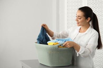 Young woman with basket full of clean laundry at table indoors