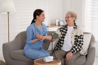 Young caregiver measuring blood pressure of senior woman in room. Home health care service