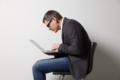 Man with bad posture using laptop while sitting on chair against grey background
