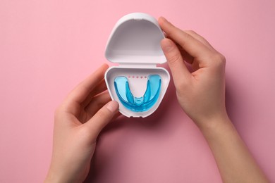 Photo of Woman holding container with mouth guard on light pink background, top view. Bite correction