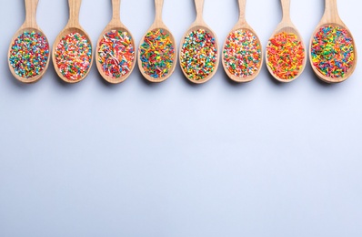 Colorful sprinkles in spoons on light grey background, flat lay with space for text. Confectionery decor