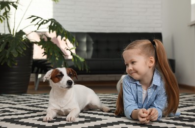 Cute little girl with her dog on carpet at home. Childhood pet