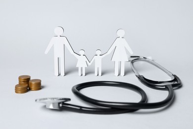 Photo of Figures of family stainding near stethoscope and coins on white background. Insurance concept