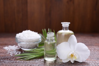 Essential oils, orchid flower and sea salt on wooden table, closeup