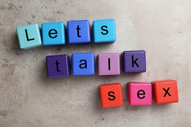 Colorful wooden blocks with phrase "LET'S TALK SEX" on stone background, flat lay