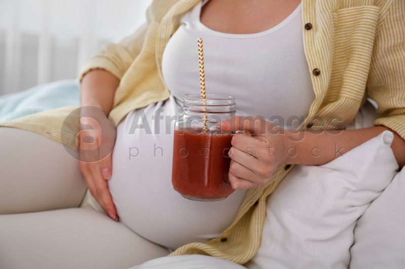 Pregnant woman with smoothie on bed, closeup. Healthy diet