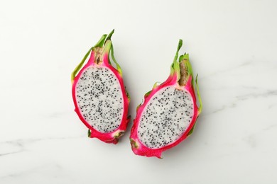 Halves of delicious dragon fruit (pitahaya) on white marble table, flat lay