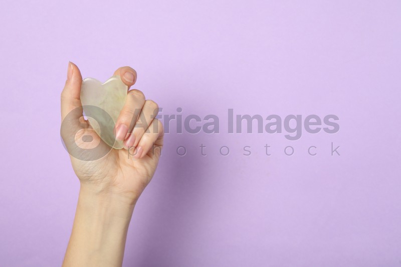 Photo of Woman with jade gua sha tool on lilac background, closeup. Space for text