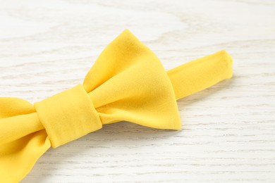 Stylish yellow bow tie on white wooden background, closeup