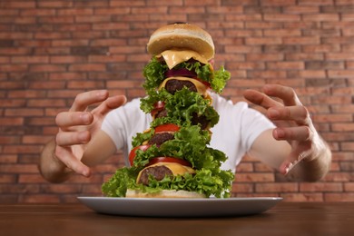 Hungry man with huge burger at wooden table