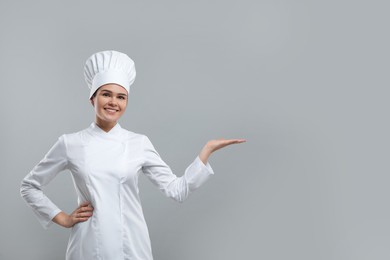 Photo of Happy female chef pointing at something on light grey background. Space for text