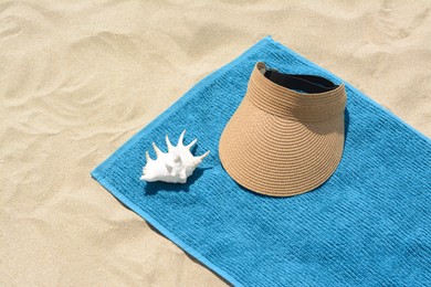 Photo of Towel, straw visor cap and seashell on sand. Beach accessories