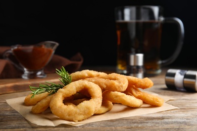 Pile of delicious crunchy fried onion rings and rosemary on wooden table