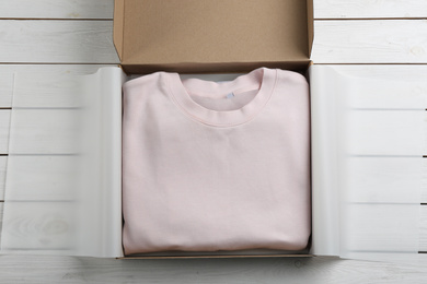 Cardboard box with clothes on white wooden background, top view