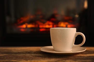 Cup with hot drink on table against fireplace, space for text