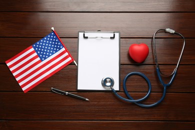 Stethoscope, red heart, clipboard and American flag on wooden table, flat lay