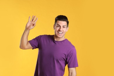 Cheerful man waving to say hello on yellow  background