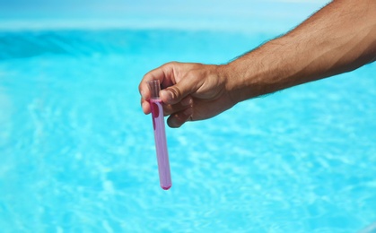 Man holding test tube with reagent near swimming pool, closeup