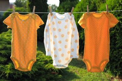 Clean baby onesies hanging on washing line in garden. Drying clothes