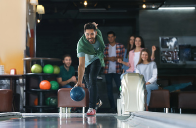 Photo of Young man throwing ball and spending time with friends in bowling club
