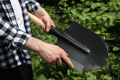 Photo of Man sharpening shovel outdoors, closeup. Gardening tools