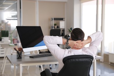 Photo of Businessman relaxing in office chair at workplace, back view