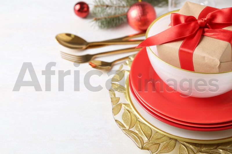 Festive dishware with gift and Christmas decorations on white table, closeup. Space for text