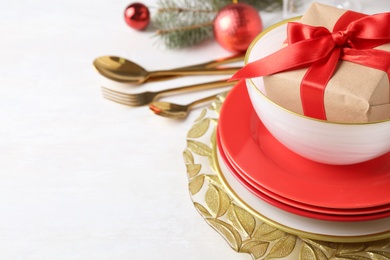Festive dishware with gift and Christmas decorations on white table, closeup. Space for text