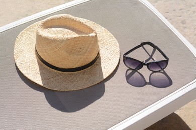 Photo of Stylish straw hat and sunglasses on grey sunbed outdoors. Beach accessories