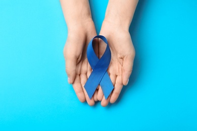 Woman holding blue awareness ribbon on color background, top view. Symbol of social and medical issues