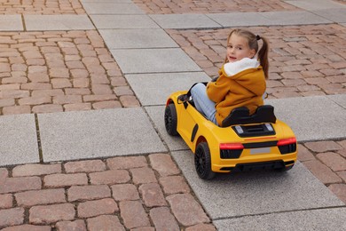 Photo of Cute little girl driving children's car on city street. Space for text