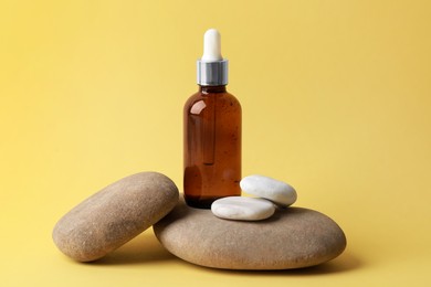 Bottle of face serum and spa stones on yellow background