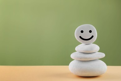 Stack of stones with drawn happy face on beige table against light green background, space for text. Zen concept