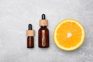 Bottles of essential oil with orange slice on grey table, flat lay
