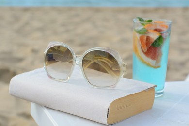 Book, sunglasses and glass of refreshing drink on beach