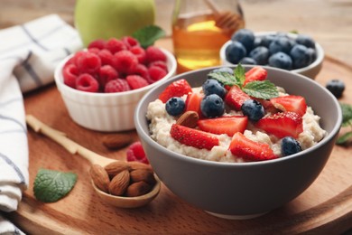 Tasty oatmeal porridge with berries and almond nuts in bowl served on wooden board