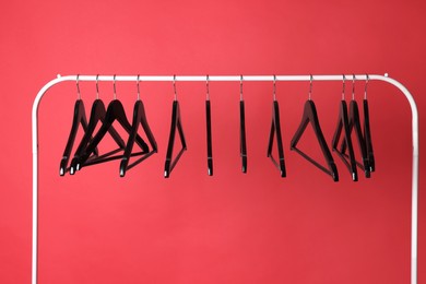 Black clothes hangers on metal rack against color background