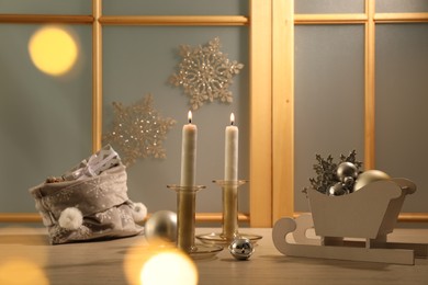 Photo of Burning candles, bag with gift boxes and festive decor on window sill indoors, bokeh effect. Christmas eve