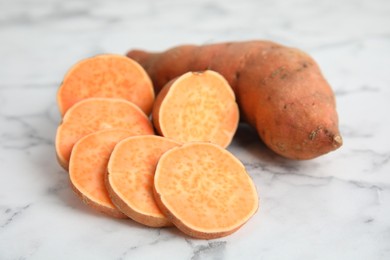 Whole and cut ripe sweet potatoes on white marble table, closeup