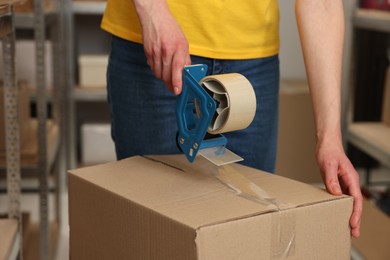 Post office worker packing box with adhesive tape indoors, closeup