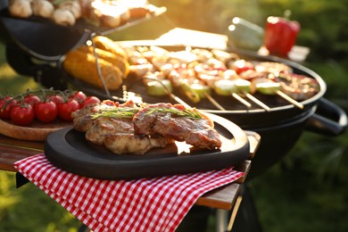 Tasty cooked meat and cherry tomatoes on table near barbecue grill outdoors