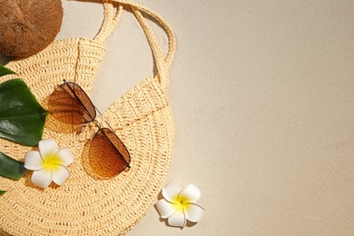 Flat lay composition with stylish sunglasses and wicker bag on sand. Space for text