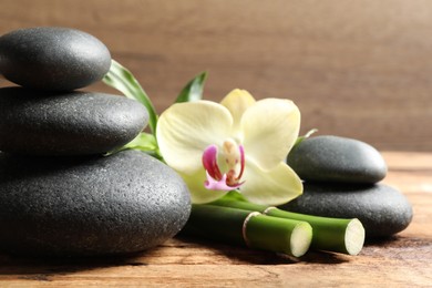 Spa stones, bamboo stems and beautiful orchid flower on wooden table, closeup