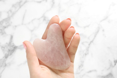 Photo of Woman with rose quartz gua sha tool at white marble table, top view